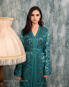 Détail du caftan broché vert orné de broderies, mettant en valeur la ceinture et la texture riche des manches avec une touche de doublure rose.