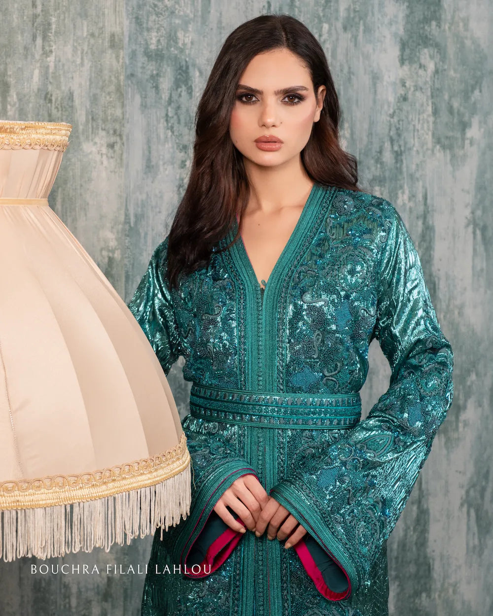 Woman wearing an emerald green brocade Moroccan caftan with intricate embroidery and fuchsia satin lining, standing gracefully in a luxurious interior.
