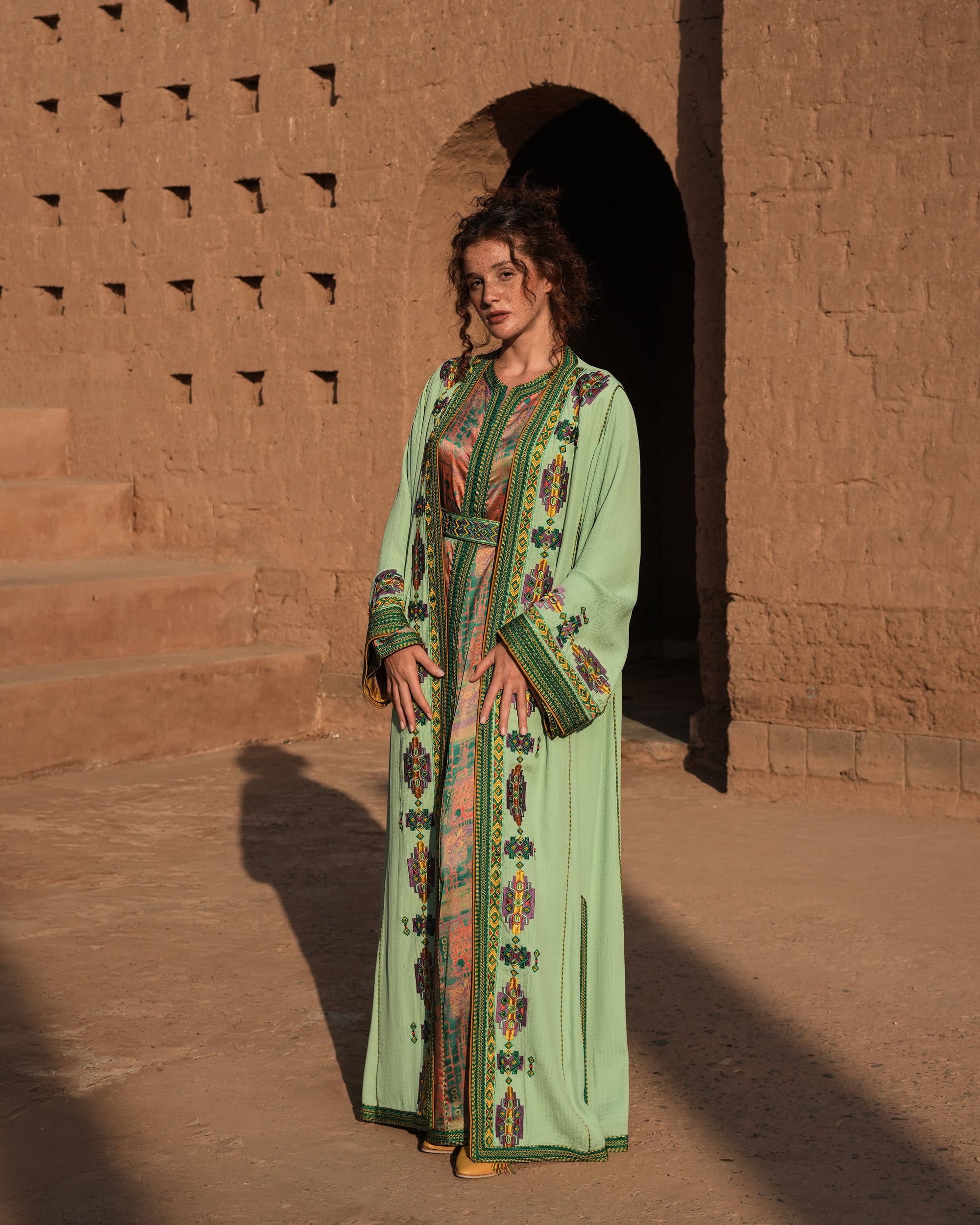 Anise Pavilion anise green Moroccan kaftan with Berber braid trims over a printed dress, full-length view