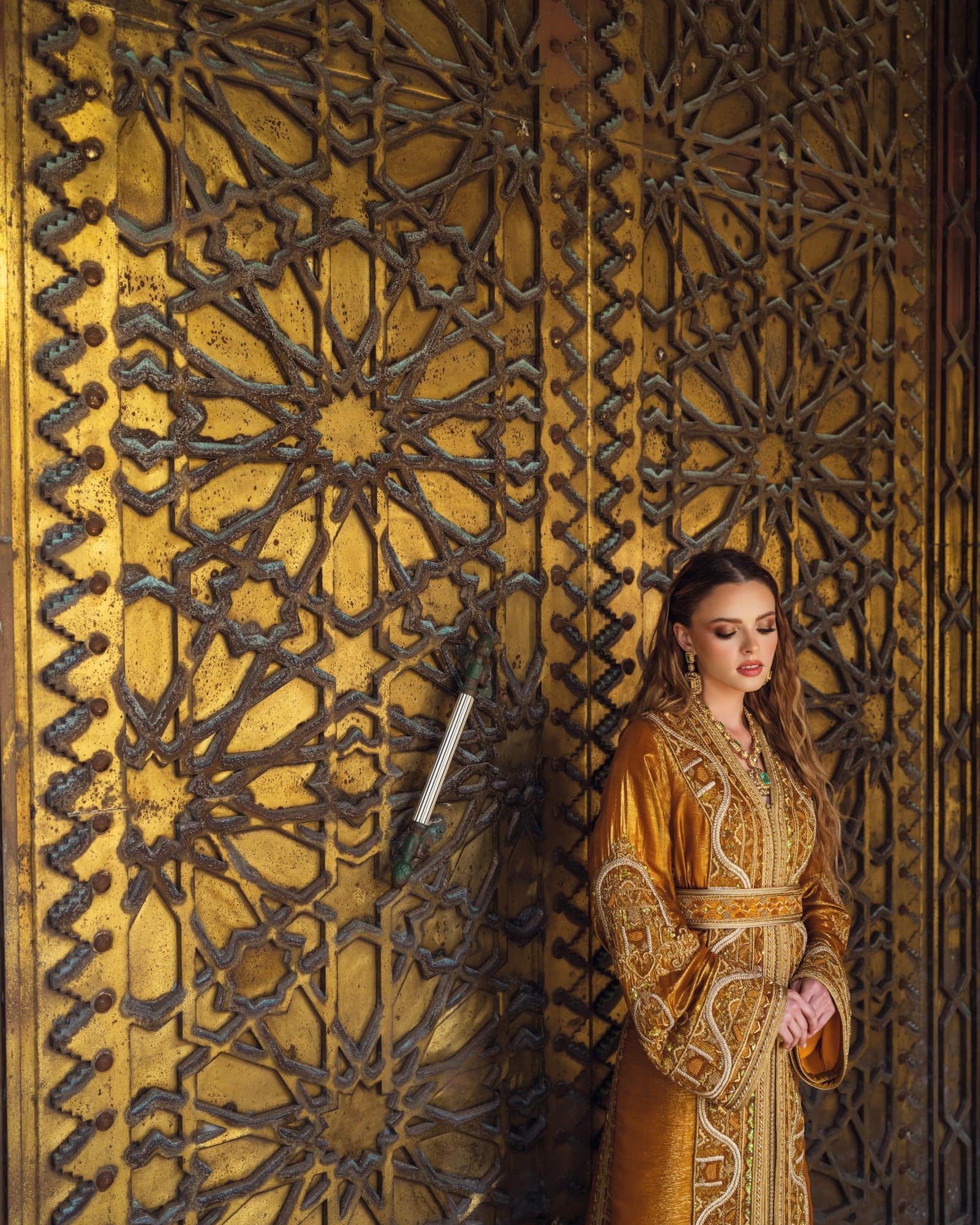Bronze Moroccan caftan beside ornate golden door with green embroidery accents