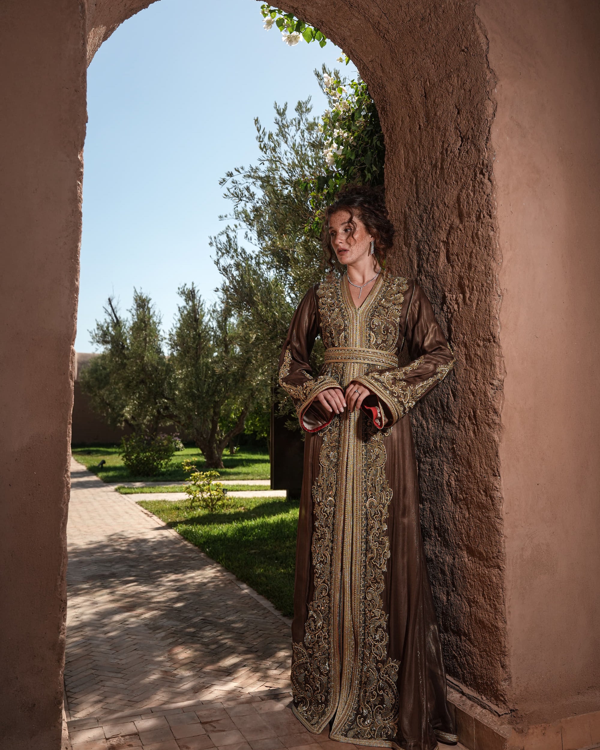 Bronze Reverie lamé organza Moroccan kaftan with gold embroidery, worn open over a champagne dress, full-length view
