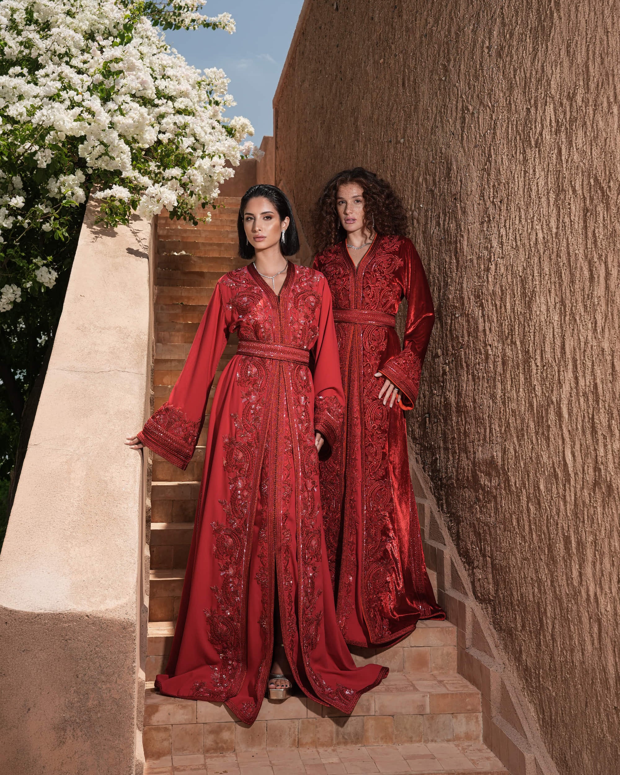 Carmine Cadence red crepe Moroccan kaftan with sequined paisley embroidery, braided belt and flared sleeves, shown alongside a second look