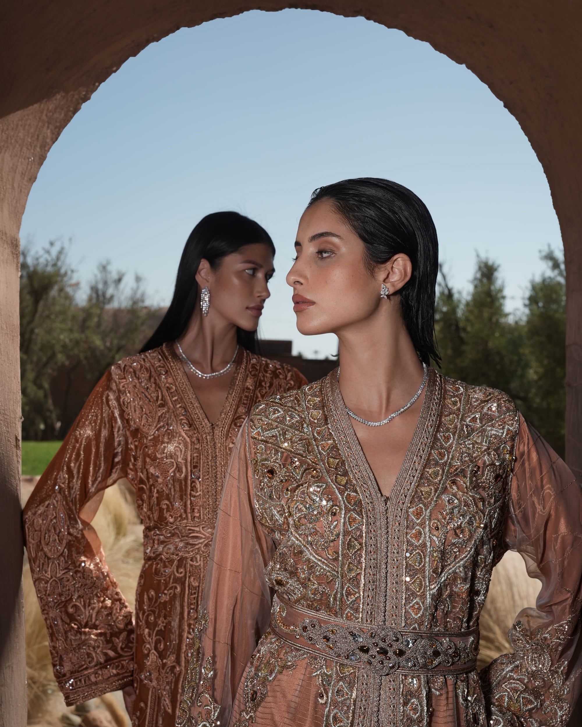 Rosewood Aurora copper-rose organza Moroccan kaftan with silver embroidery and jewelled belt, shown alongside a second look