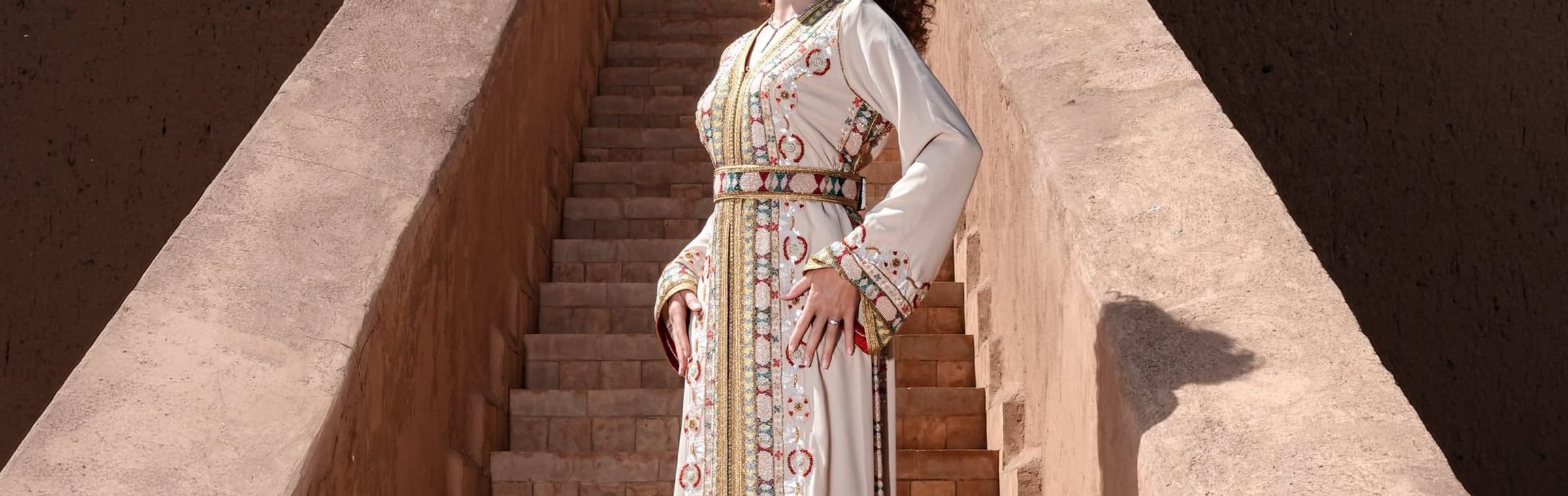 Ecru crepe Moroccan kaftan belted at the waist on a Marrakech staircase