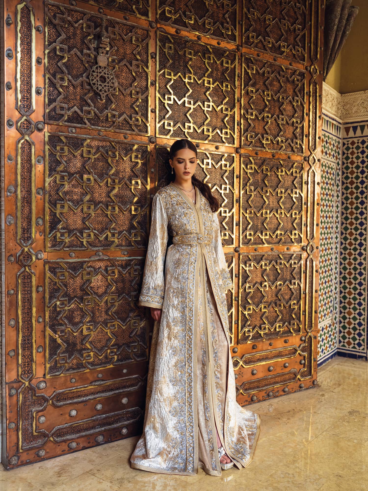 Ivory gold Moroccan kaftan with ornate embroidery before carved door